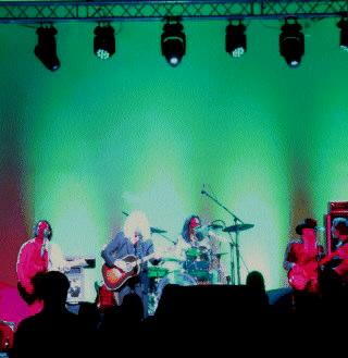 (Image: The Band on Stage at The Steel Wheels Museum Venue
  with Pink Front, and Green & Blue Back/Screen Lighting)